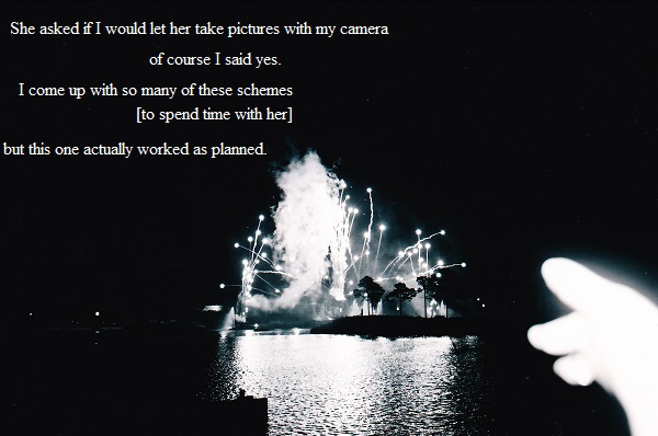 Hand pointing to fireworks exploding above the water