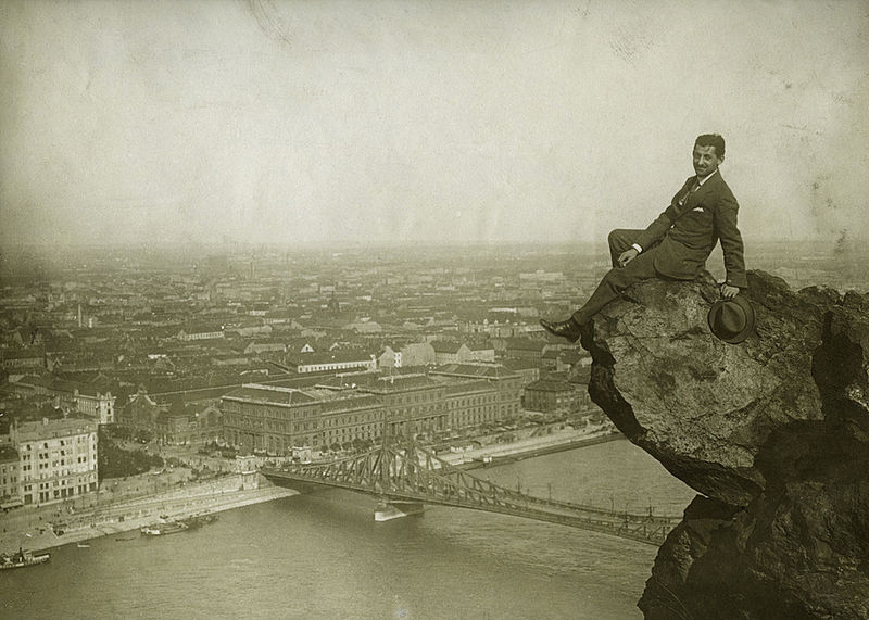 Image of a man sitting on a boulder overlooking a city